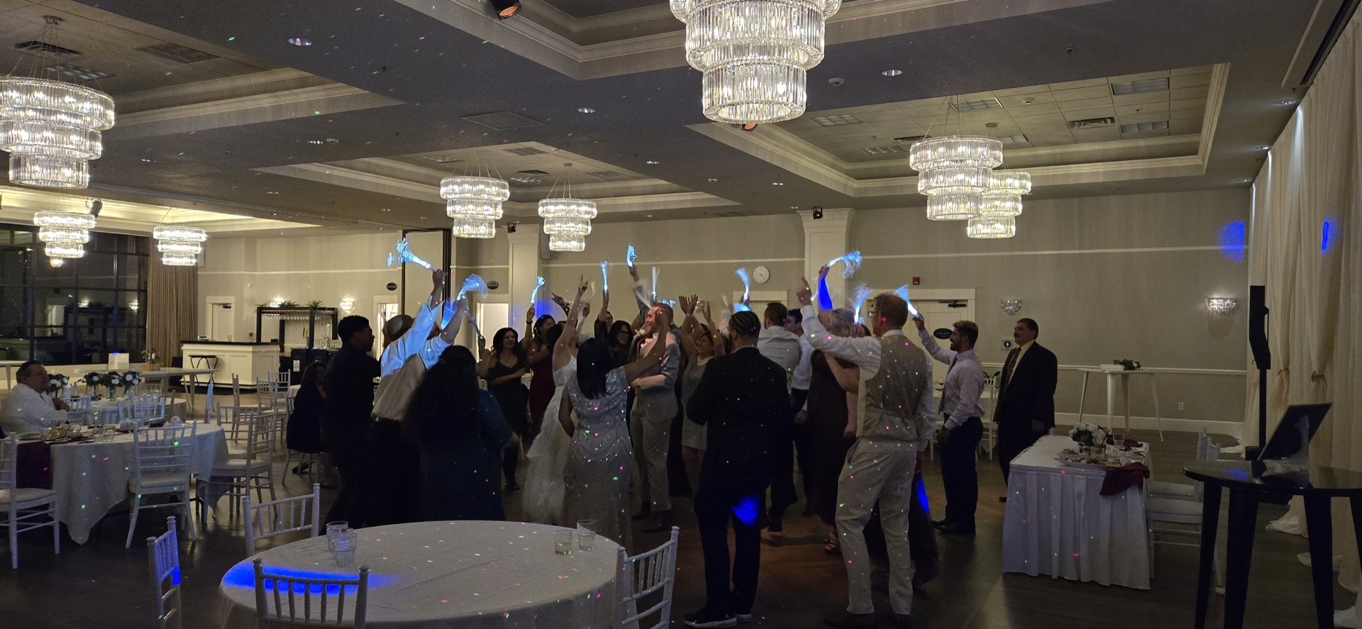 Guests dance with glow props at an Apogee event DJ party in a chandelier-lit ballroom
