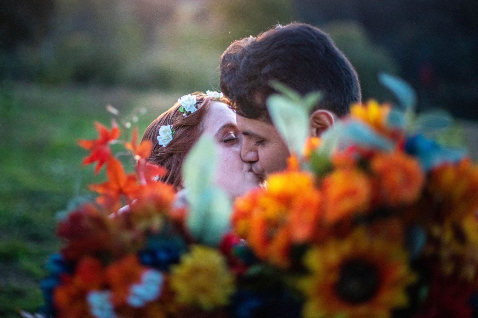 Bride and groom kiss behind an out-of-focus foreground of orange and yellow bouquet flowers