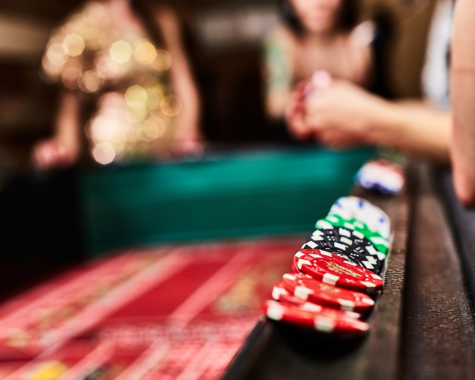 Stacks of red, black and green chips on the rail of a craps table while guests play behind