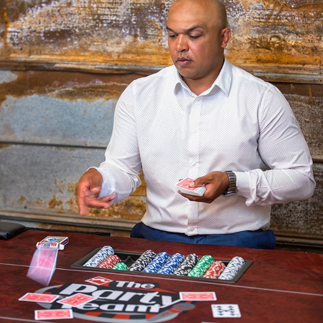 Dealer shuffles cards at a poker table with racks of chips at a casino party