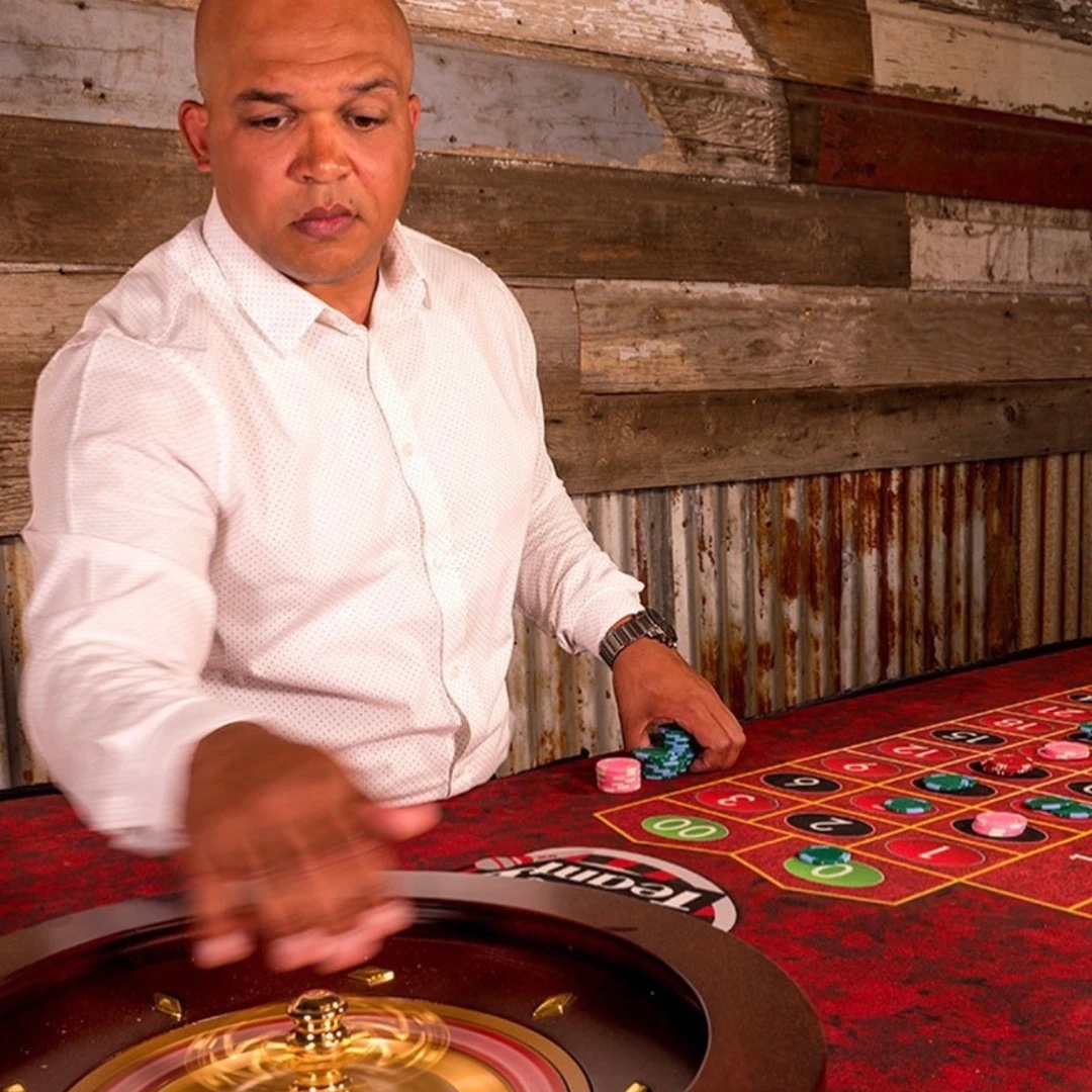 Dealer in a white shirt spins the roulette wheel at a casino party table stacked with chips