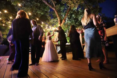 A bride and groom dance at night with string lights above.