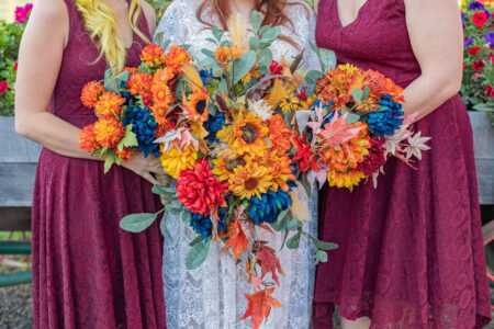 Vibrant red, blue, orange, flowers are arranged by two bridesmaids and a bride show off their bouquets. The three are pressed together to appear as one giant bouqet.