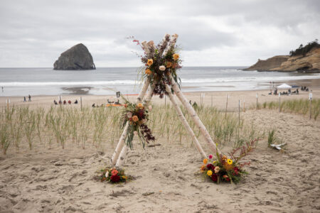 An arched triangle wedding ceremony setup on the beach in front of Haystack Rock in Oregon.