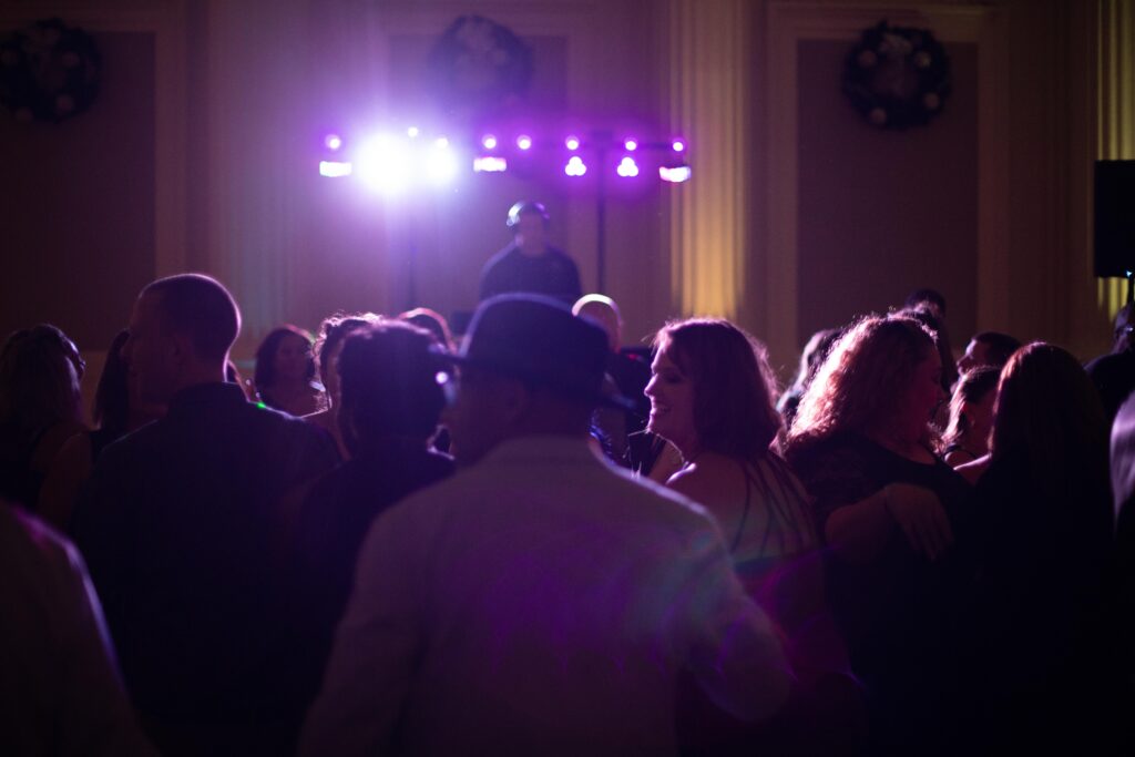 Event guests pack a dance floor with a DJ and dance lights in the background.