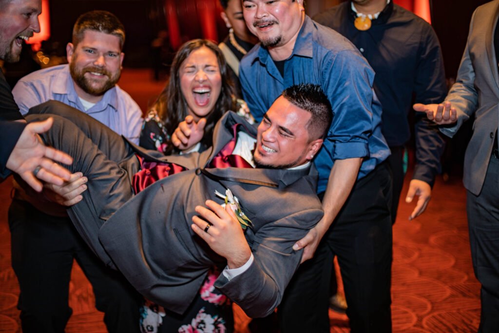 A man is held up on the dance floor with a huge smile on his face.