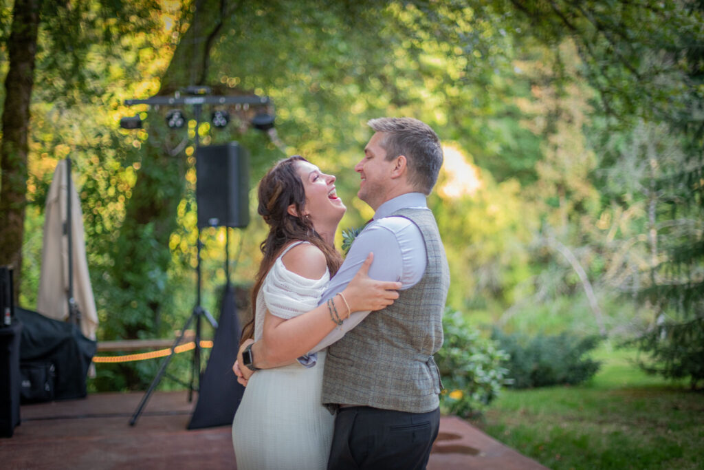 a bride and her father dance. In the background are green trees in the PNW.