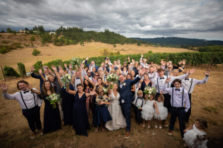 All wedding guests group photo waving on Oregon vineyard hillside with rows of grapevines