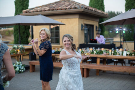 Bride dancing with wine glass at outdoor Oregon wedding reception DJ setup visible in background