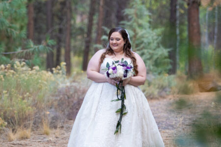 Bride in wedding gown walking through forest holding bouquet at Oregon outdoor wedding