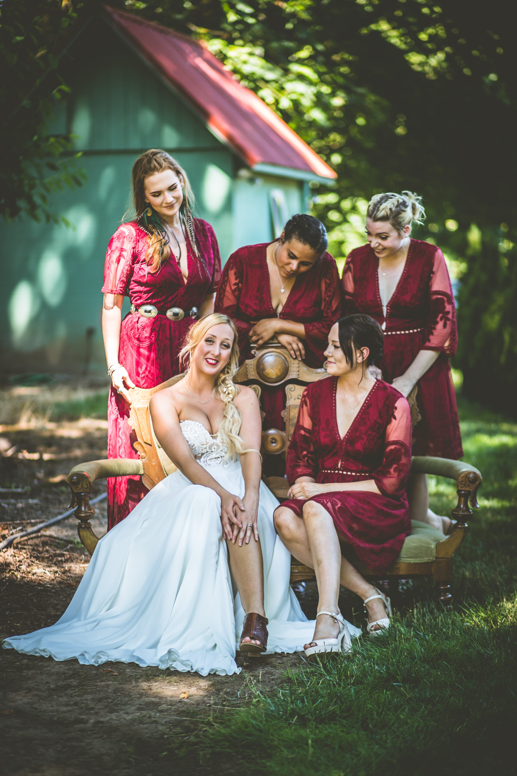 A bride poses with her bridesmaids with a green cabin in a tree covered area