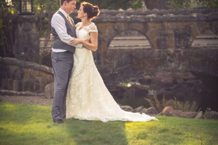 Bride and groom embracing at stone bridge in garden at golden hour Oregon wedding photography Wes Fisher
