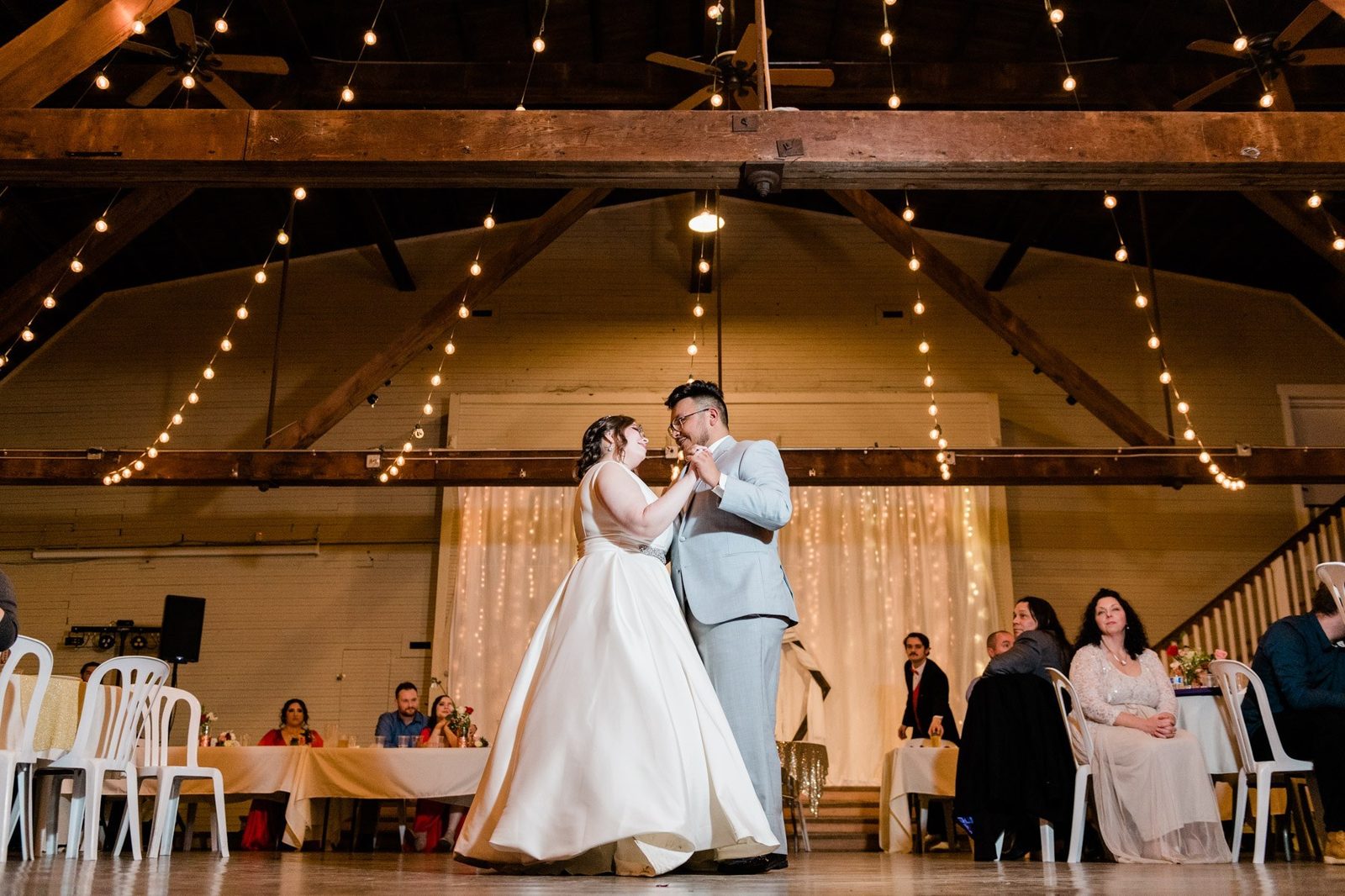 Bride and groom first dance in barn with string lights